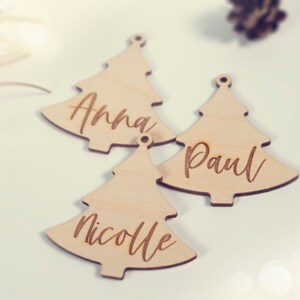 May include: Three wooden Christmas tree ornaments with the names Anna, Paul, and Nicole engraved on them.