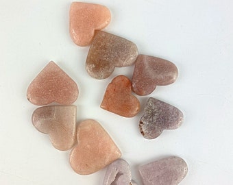 May include: A collection of ten heart-shaped polished stones in shades of pink, brown, and white. The stones are arranged in a loose cluster on a white background.