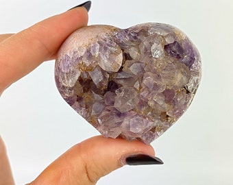 May include: A heart-shaped amethyst crystal with a druzy finish. The crystal is a deep purple color and has a natural, rough texture.