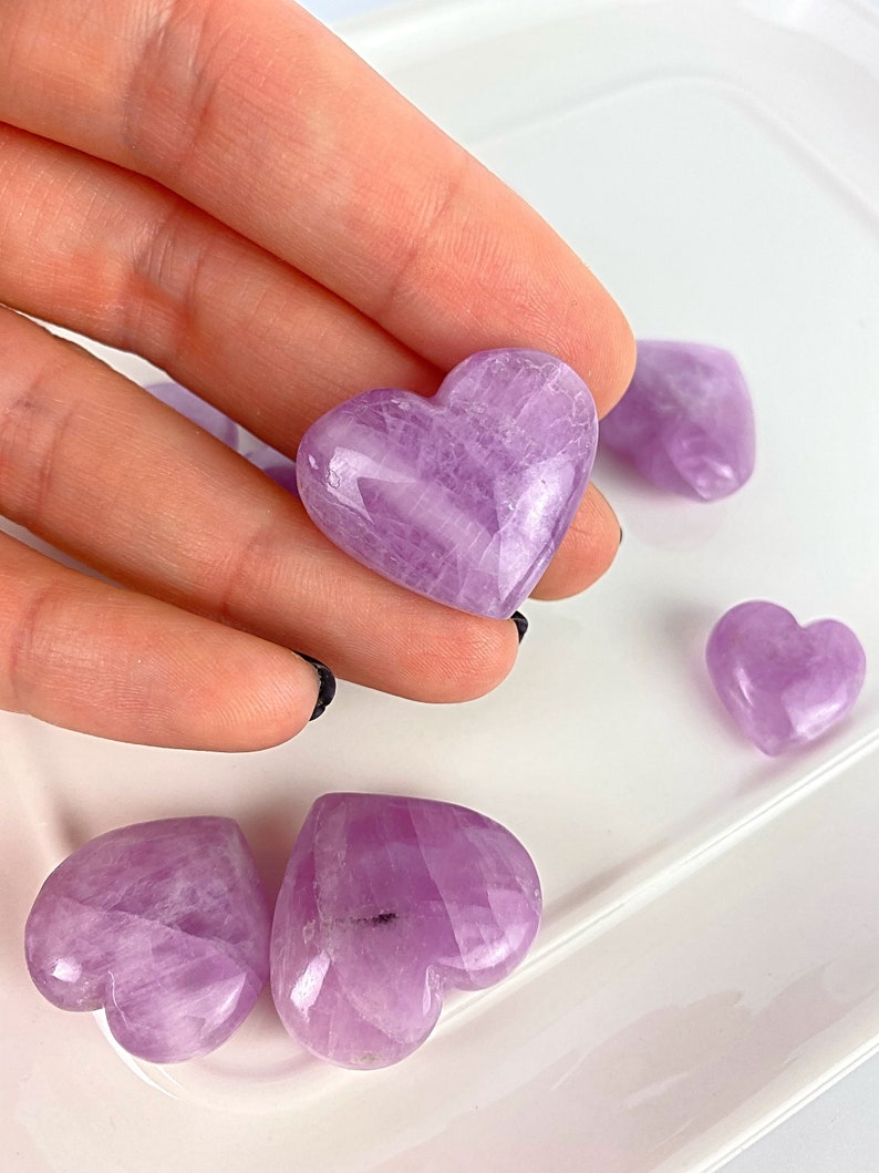 May include: A collection of polished amethyst heart-shaped stones. The stones are a light purple colour and have a smooth, polished finish.