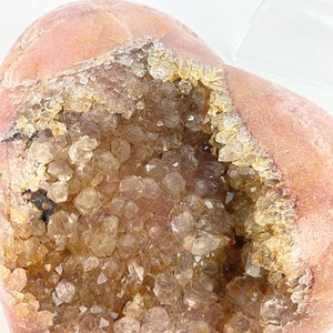 May include: A heart-shaped geode with a pink exterior and a cavity filled with clear quartz crystals.