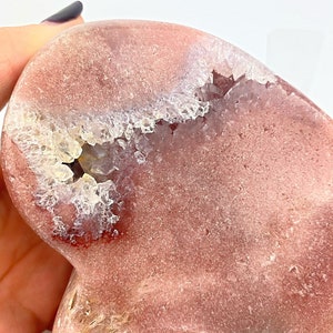 May include: A heart-shaped pink agate geode with a natural crystal formation. The geode has a smooth, polished exterior and a rough, textured interior with a white crystal cluster.