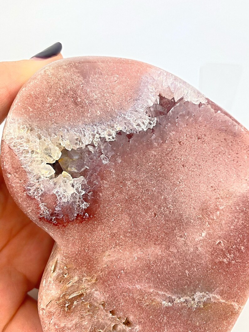 May include: A heart-shaped pink agate geode with a natural crystal formation. The geode has a smooth, polished exterior and a rough, textured interior with a white crystal cluster.
