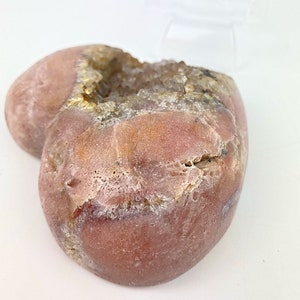 May include: A heart-shaped geode with a pink exterior and a white crystal interior. The geode is smooth and has a natural, organic shape.