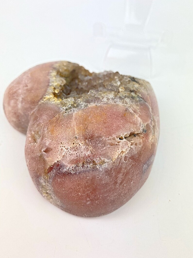 May include: A heart-shaped geode with a pink exterior and a white crystal interior. The geode is smooth and has a natural, organic shape.