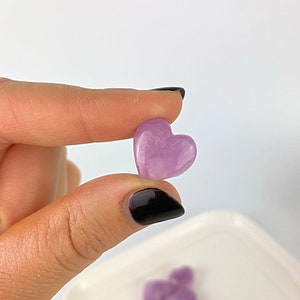 May include: A collection of small, heart-shaped amethyst crystals in shades of purple. The crystals are arranged on a white plate.