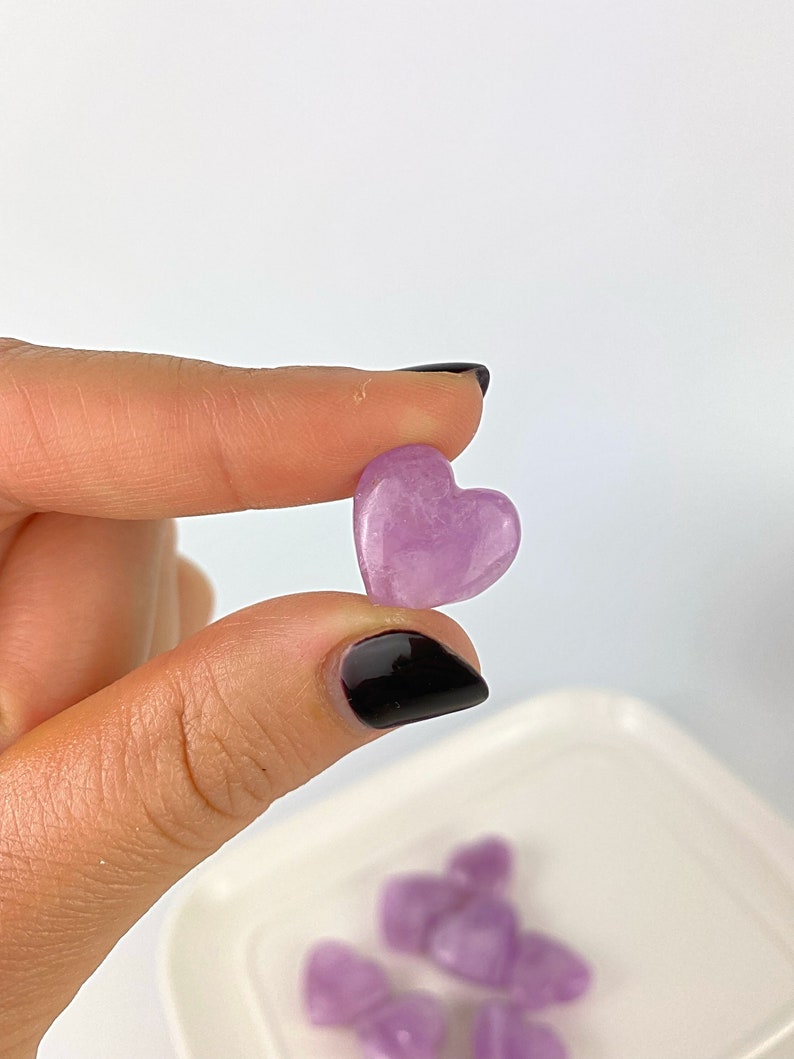May include: A collection of small, heart-shaped amethyst crystals in shades of purple. The crystals are arranged on a white plate.
