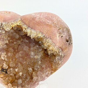 May include: A heart-shaped geode with a pink exterior and a cavity filled with clear quartz crystals. The crystals are clustered together and have a light brown color.
