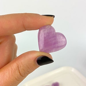 May include: A small, heart-shaped, polished amethyst crystal with a light purple hue. The crystal has a smooth, polished surface and is a light purple colour.