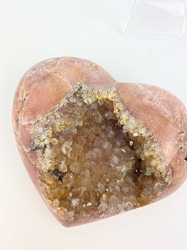 May include: A heart-shaped geode with a pink exterior and a hollow interior filled with clear quartz crystals.