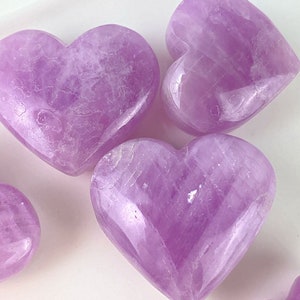 May include: Four heart-shaped amethyst crystals in various sizes, polished to a smooth, shiny finish. The crystals are a light purple colour and have a translucent appearance.