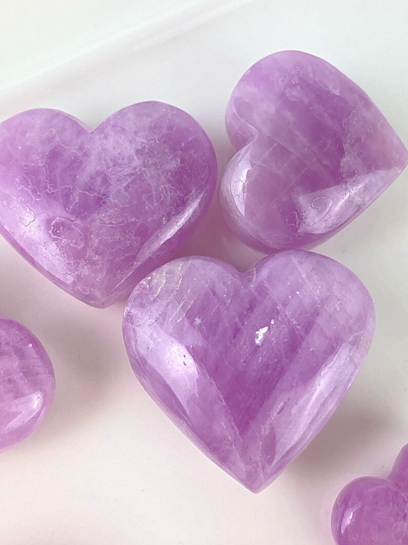 May include: Four heart-shaped amethyst crystals in various sizes, polished to a smooth, shiny finish. The crystals are a light purple colour and have a translucent appearance.