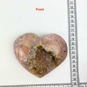 May include: A heart-shaped stone with a large opening filled with clear quartz crystals. The stone is a light pink color with brown markings.