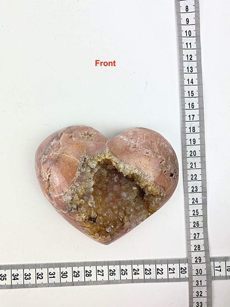 May include: A heart-shaped stone with a large opening filled with clear quartz crystals. The stone is a light pink color with brown markings.