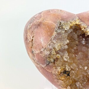 May include: A heart-shaped geode with a pink exterior and a cavity filled with clear quartz crystals.