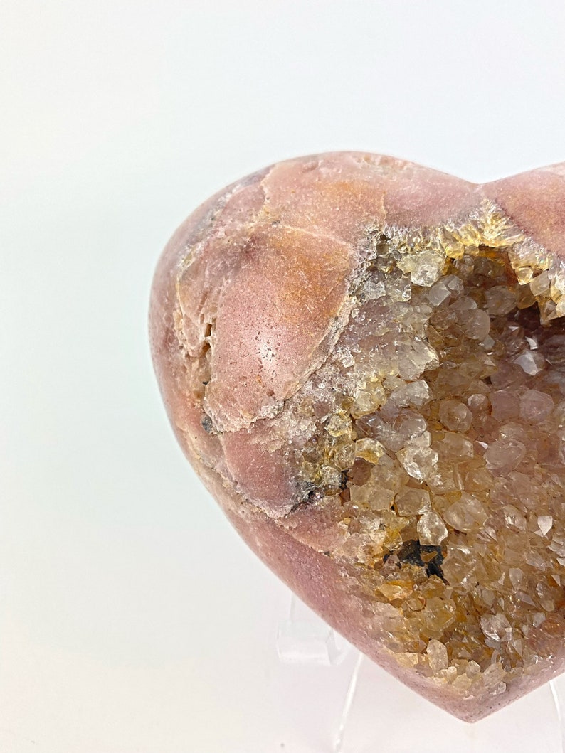 May include: A heart-shaped geode with a pink exterior and a cavity filled with clear quartz crystals.