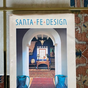 May include: A book titled "Santa Fe Design" with a photograph of a doorway with a blue wall, a rug, and two blue ceramic pitchers on the cover.