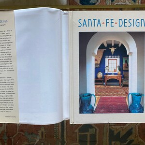 May include: A book cover with the title "Santa Fe Design" in a white font on a white background. The cover features a photograph of a doorway with a blue wall and a rug on the floor. There are two blue vases on either side of the doorway.