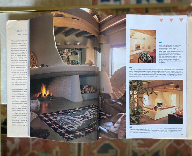 May include: A living room with a large fireplace and a rug with a southwestern design. The room has a beamed ceiling and a large window. The text in the image reads "Left: This living room, Westwood Architects created a contemporary space with a monumental fireplace, a concealed television, and a large rug.  The room has a comfortable, triangle-shaped banquette and a low, deep sofa to lean toward.  There is a deep, soft bed that crowns the seating platform, and handsome plantings."