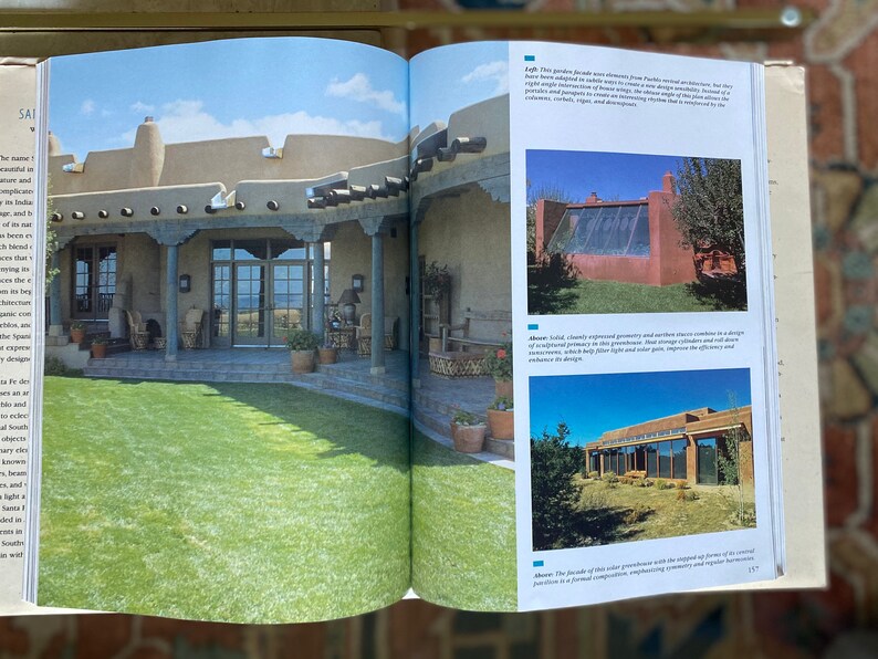 May include: A book open to a page with a picture of a house with a large yard and a description of the house's design. The text on the page describes the house's design and the use of natural materials.