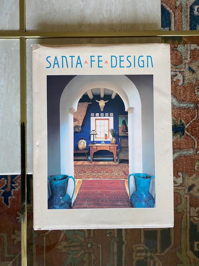 May include: A book titled "Santa Fe Design" with a photograph of a doorway with a blue wall, a rug, and two blue ceramic pitchers on the cover.