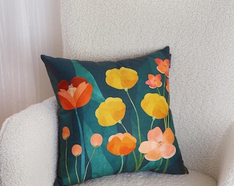 May include: A teal blue throw pillow with a floral pattern featuring orange, yellow, and pink flowers. The pillow is sitting on a white fluffy chair.