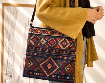 May include: A square crossbody bag featuring a dark blue base with a multi-colored geometric pattern in red, orange, and green. The bag has a long, thin dark strap and a repeating diamond and floral motif across the front surface of the fabric.