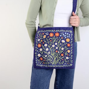 May include: A blue canvas tote bag with a floral print featuring a variety of flowers in shades of orange, white, and yellow. The bag has a long strap and is worn over the shoulder.