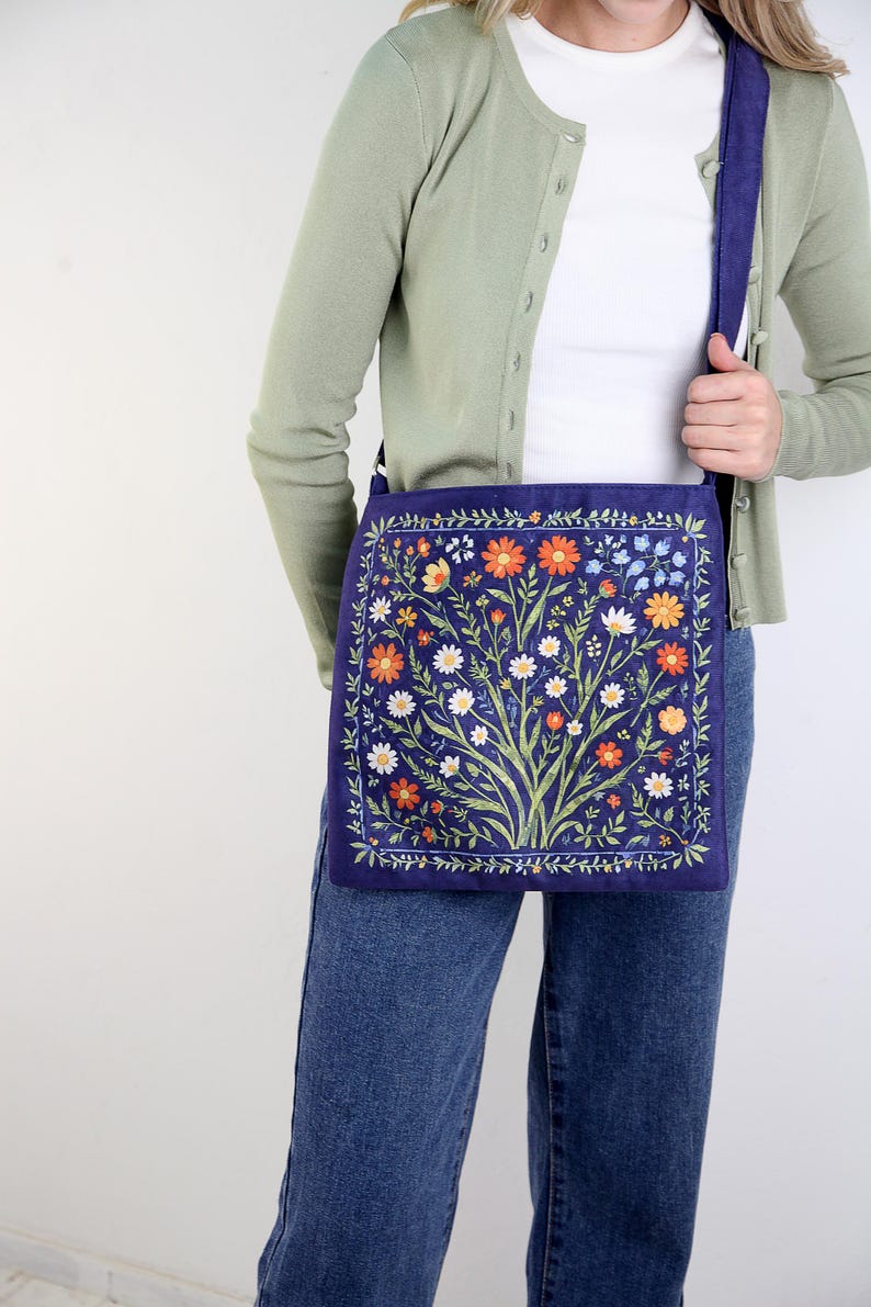 May include: A blue canvas tote bag with a floral print featuring a variety of flowers in shades of orange, white, and yellow. The bag has a long strap and is worn over the shoulder.