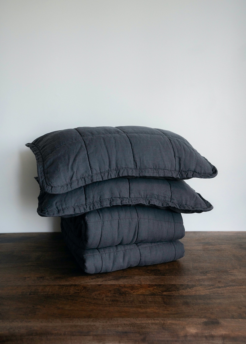 May include: A stack of three dark grey quilted throw pillows with a ruffled edge.