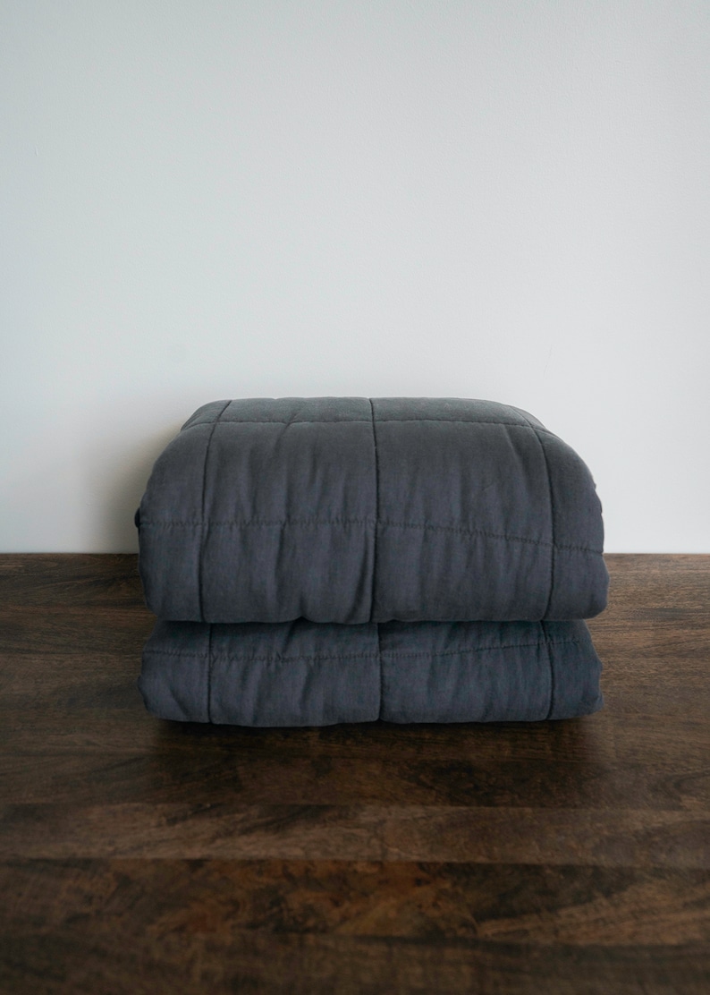 May include: A dark grey quilted blanket folded in half on a wooden surface.