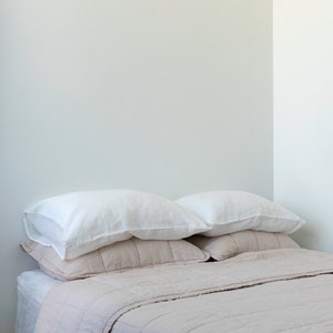 May include: A light brown quilted bedspread with two white pillows on top. The bedspread is made of a soft, textured fabric.