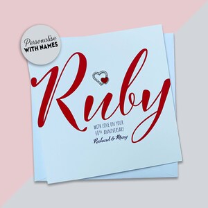 May include: A light blue card with the word "Ruby" in red cursive lettering. A small red heart with silver accents is above the word. The text "With love on your 40th Anniversary" is below the word "Ruby" and the names "Richard & Mary" are below that.