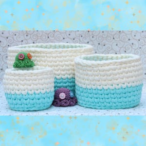 Peut inclure: Trois paniers en crochet de couleur blanche et bleu clair avec une petite pieuvre en crochet de couleur violette. Les paniers sont faits avec un point texturé et ont une forme arrondie.