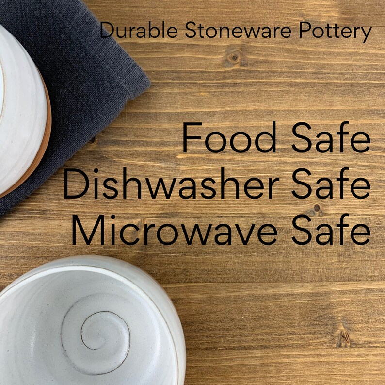 May include: Two white ceramic bowls on a wooden surface. The bowls are food safe, dishwasher safe, and microwave safe. Durable stoneware pottery.