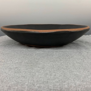 May include: A black ceramic bowl with a brown rim. The bowl is sitting on a gray fabric surface.