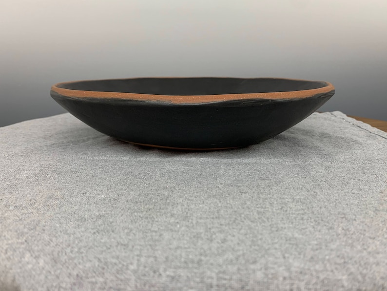 May include: A black ceramic bowl with a brown rim. The bowl is sitting on a gray fabric surface.