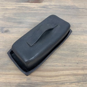 May include: Black ceramic butter dish with a lid and a handle. The dish is made of a smooth, matte black ceramic.
