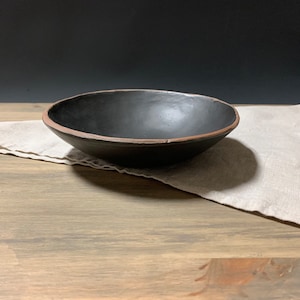 May include: A black ceramic bowl with a brown rim, sitting on a wooden surface with a linen napkin.