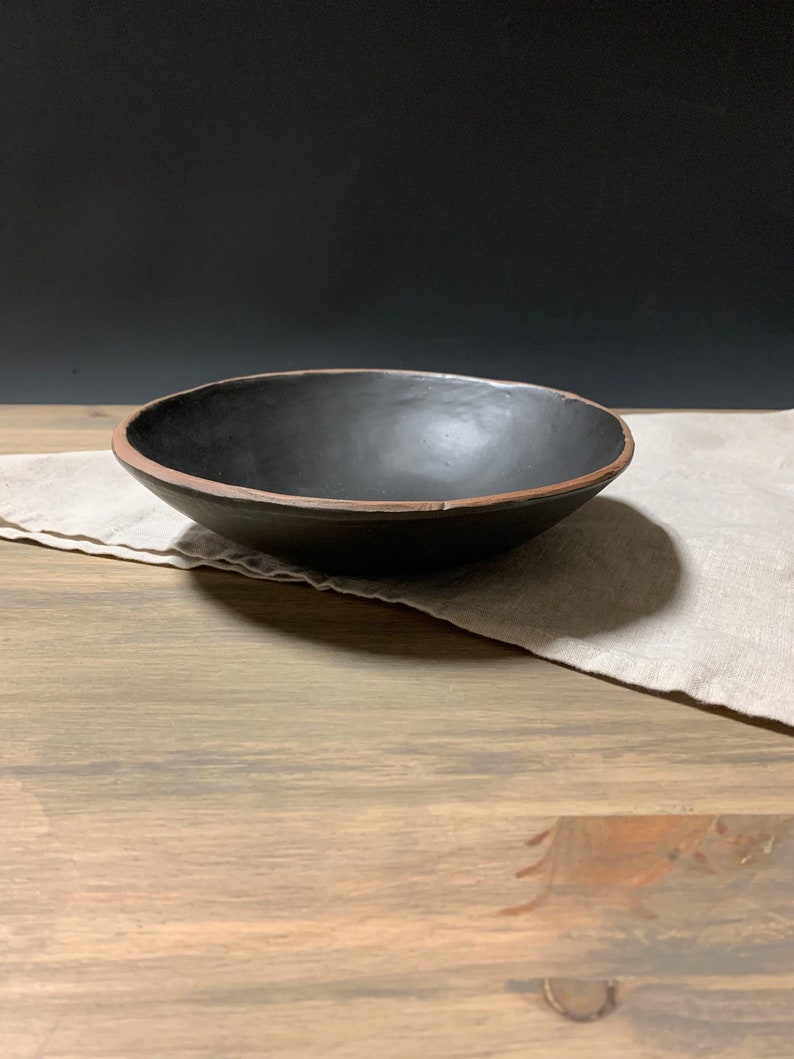 May include: A black ceramic bowl with a brown rim, sitting on a wooden surface with a linen napkin.