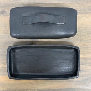 May include: A black rectangular ceramic tray with a matching lid. The lid has a handle.