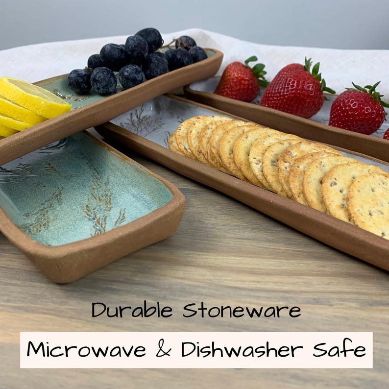 May include: A set of three rectangular stoneware serving trays with a light brown rim and a light blue interior. The trays are filled with grapes, strawberries, lemon slices, and crackers. The text "Durable Stoneware" and "Microwave & Dishwasher Safe" is displayed.