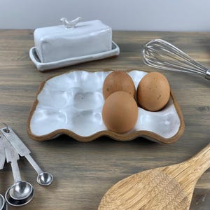May include: White ceramic egg holder with three brown eggs. The holder has a wavy edge and is made in a rustic style.