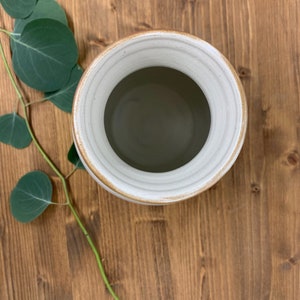May include: White ceramic vase with a brown rim. The vase is empty and has a smooth, rounded interior.