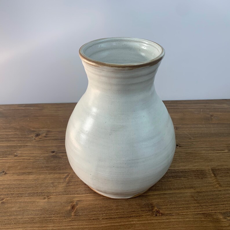 May include: A white ceramic vase with a brown rim. The vase has a rounded body and a narrow neck.
