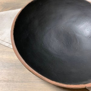 May include: A large, black ceramic bowl with a slightly raised rim. The bowl is empty and has a matte finish.