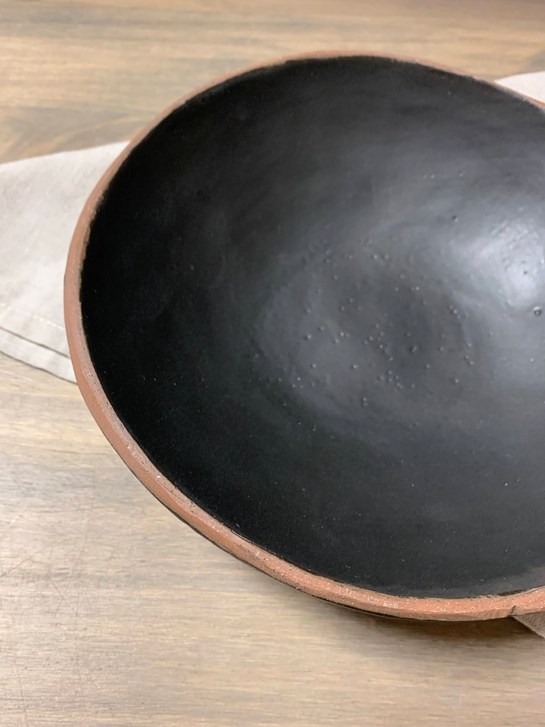 May include: A large, black ceramic bowl with a slightly raised rim. The bowl is empty and has a matte finish.