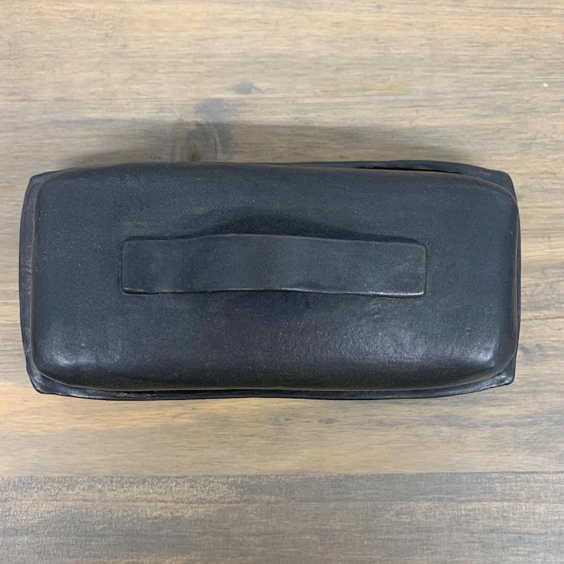 May include: Black ceramic butter dish with a handle. The dish has a textured surface.