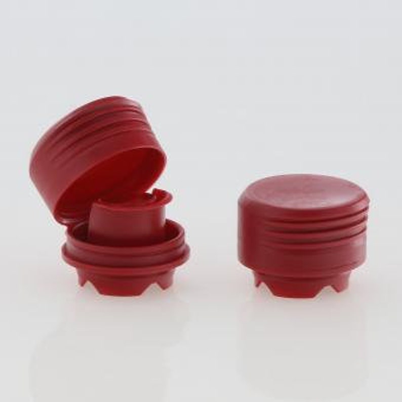 Puede incluir: Dos tapones de botella de pl&aacute;stico rojo con un dise&ntilde;o acanalado. El tap&oacute;n de la izquierda est&aacute; abierto, revelando un inserto de pl&aacute;stico blanco.