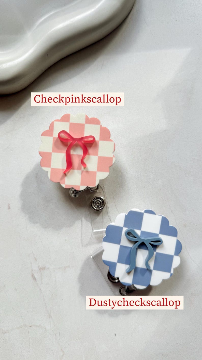 Pu&ograve; includere: Due porta badge decorativi. Uno &egrave; a scacchi rosa e bianchi con un fiocco rosa, l'altro &egrave; a scacchi blu e bianchi con un fiocco blu. Il testo "Checkpinkscallop" e "Dustycheckscallop" &egrave; stampato sull'immagine.
